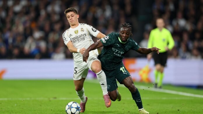 Arda Gueler of Real Madrid is challenged by Jeremy Doku of Manchester City during the UEFA Champions League 2025/26 League Phase MD6 match between Real Madrid C.F. and Manchester City at Estadio Santiago Bernabeu on December 10, 2025 in Madrid, Spain.